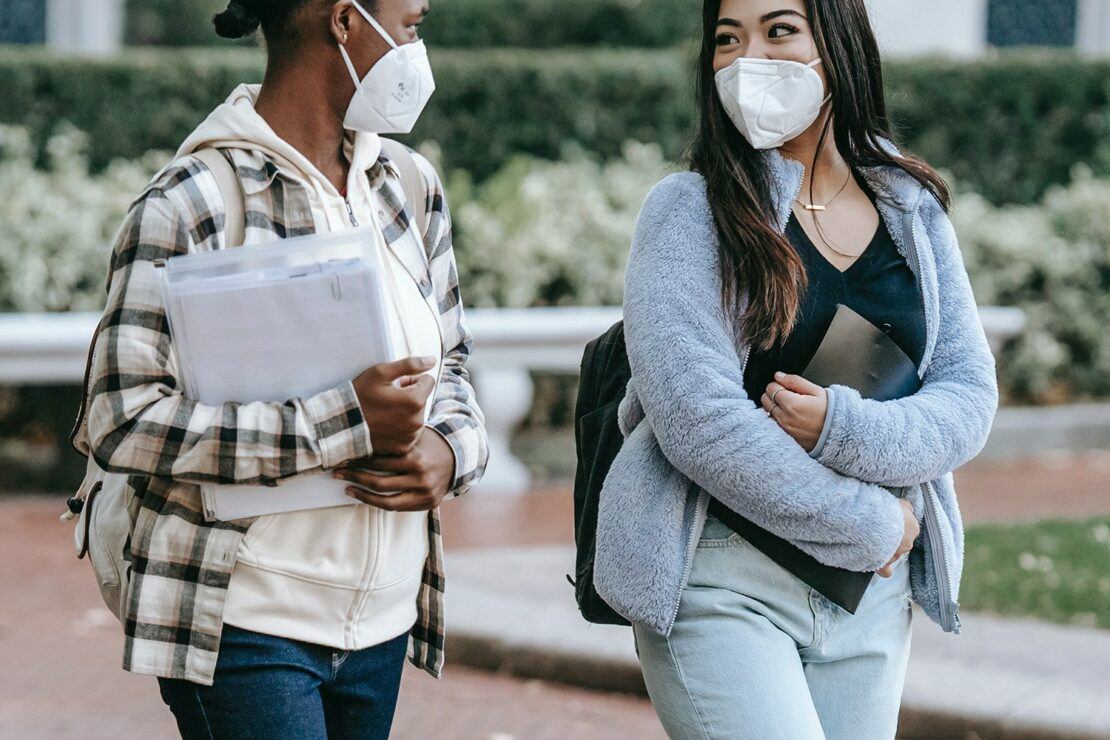 two students carrying books wearing masks