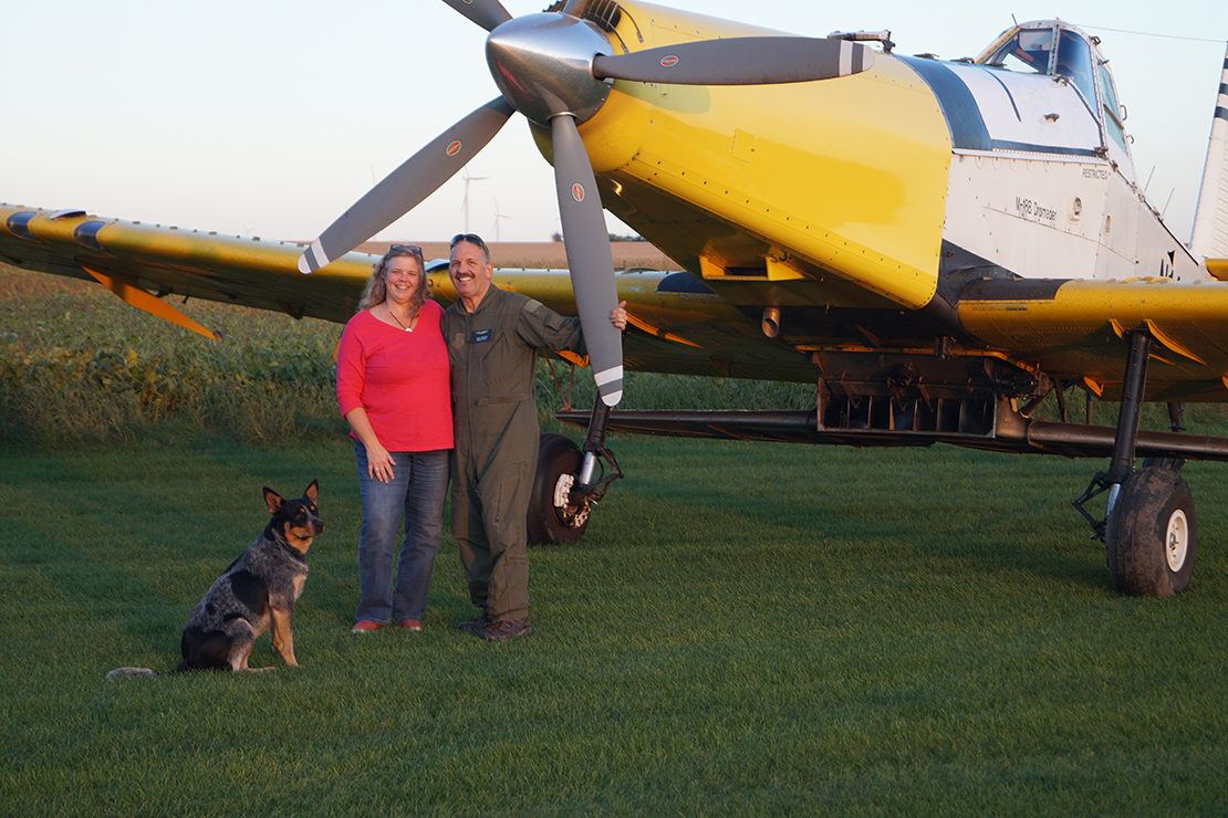 Hamilton family and their dog standing in front of farm field with their cover crop plane in the background