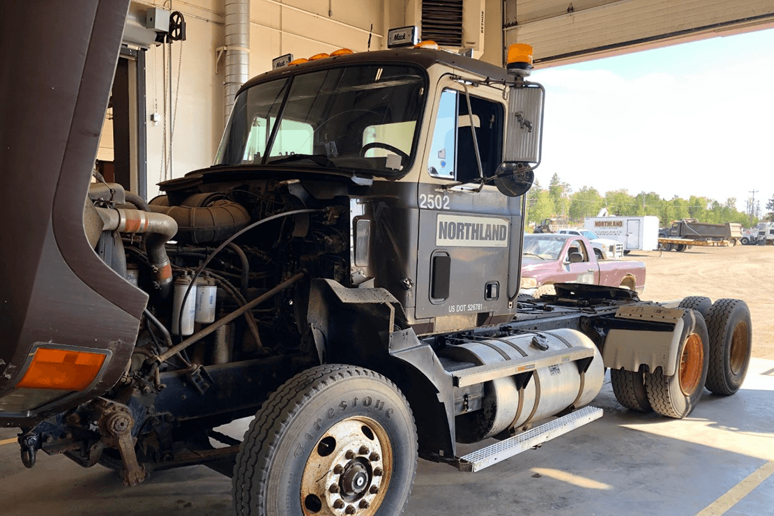 Black class 8 diesel truck with hood open so engine can be viewed.