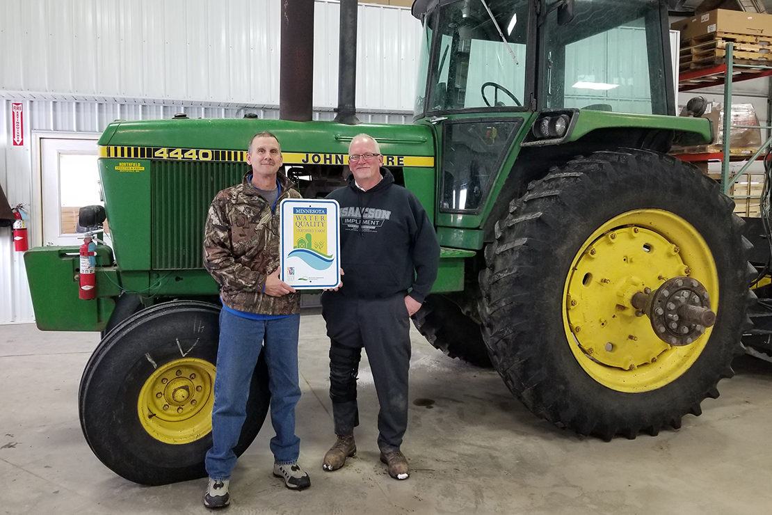 Bob and Rich Sommers standing in a shed in front of a green John Deer tractor