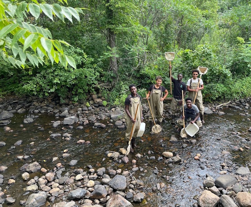 five youth wearing waders in a stream and holding nets