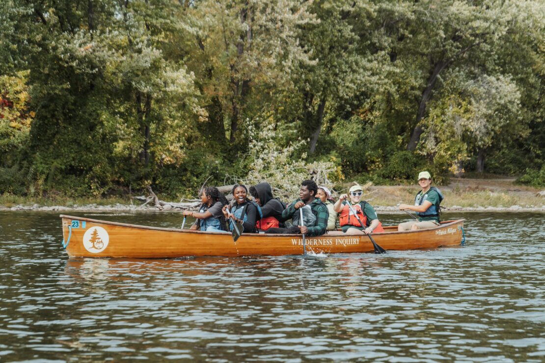 A group of adults and teenagers paddling a canoe down the Mississippi River.