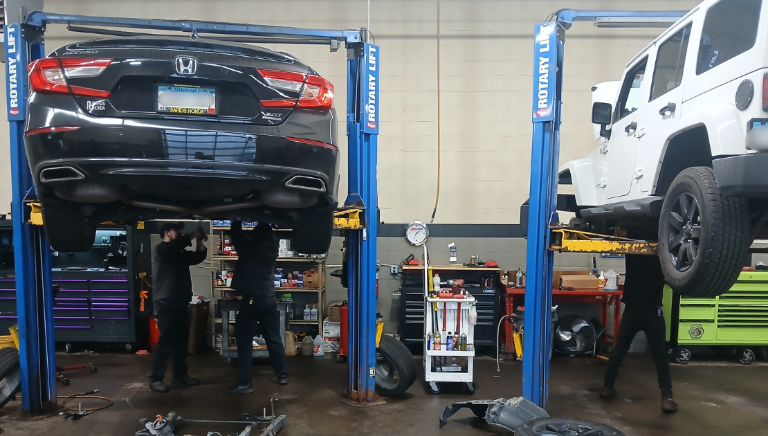Two cars suspended on lifts being worked on by mechanics.